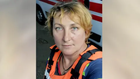 Inna Lytvynenko Inna Lytvynenko is wearing her bright orange body armour and standing in front of an ambulance. 