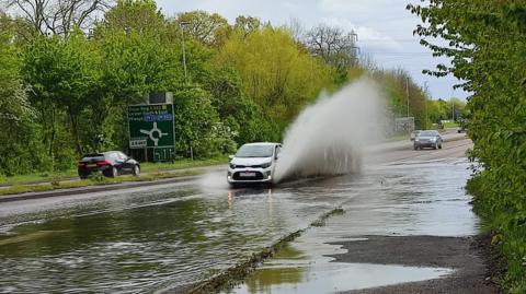 Spray launched high into the air as a car drives through flood waters.
