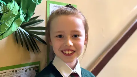 Child age 9 is smiling at camera, she is in her school hallway.