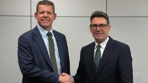 A formal picture of Rhun ap Iorwerth and Andy Burnham shaking hands