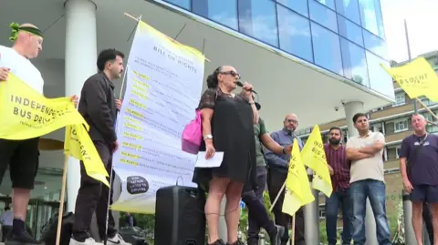 A group of people holding banners, one is speaking into a mic 