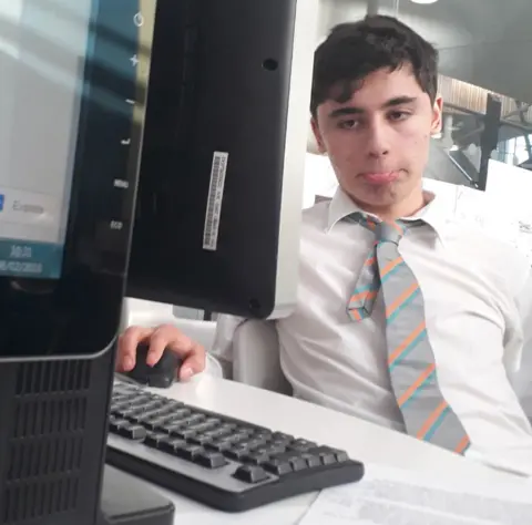 Dexter Couchman Daniel Khalife is pictured at school wearing a shirt and striped tie with top button undone, while using a computer in a classroom.