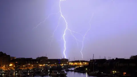 Getty Images A fork of lighting flashes over Sovereign Harbour, Eastbourne, at night. Boats and the seafront buildings in the foreground.