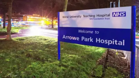 External view of Arrowe Park Hospital with a sign which reads: "Welcome to Arrowe Park Hospital"