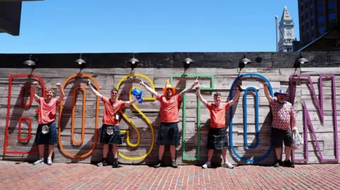 PA Media A group of football fans wearing Scotland tops standing in front of a multi coloured Boston sign. 