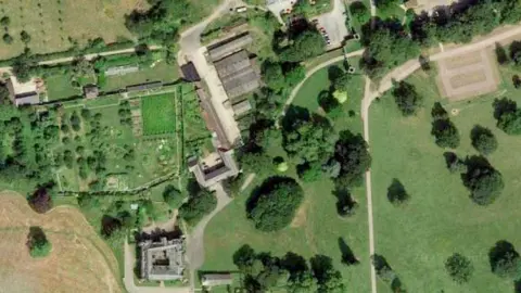 An aerial view of the Croft Castle site, showing the castle at the bottom of the photograph and the Home Farm buildings above it. There is greenery around the site.