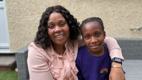 Elina and her daughter Helen. Elina has her arm around Helen. Elina is wearing a peach coloured chiffon top. Helen is wearing a purple school tshirt 