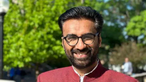 BBC Badar Khan Suri, a scholar of conflict studies, was arrested on 17 March over terror charges. He is seen wearing a maroon jacked over a white shirt and  spectacles, with trees in the background.