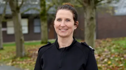 An image of sergeant Zoe Bradstreet from Surrey Police. Zoe, whose hair is tied up, is wearing a black police top.