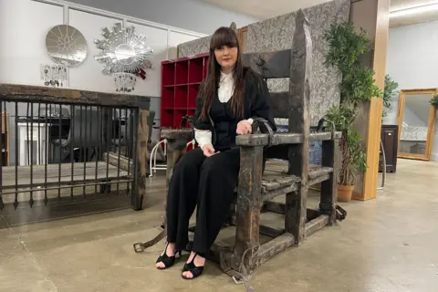 BBC Sian Cullen sitting in her interrogation chair with the cage in the background