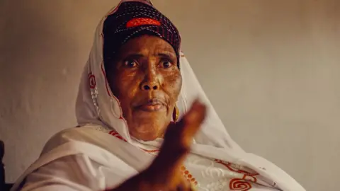 Netflix Binti Ali Wardhere with a white headscarf looks like she is in mid-conversation as she gesticulates with her hand that is out of focus in the foreground.