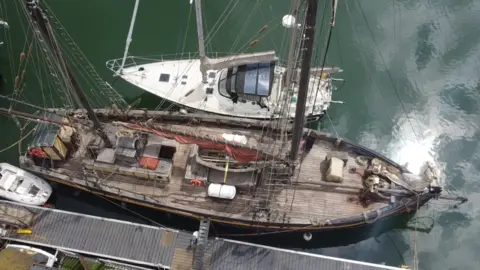 Jamie Niblock/BBC An aerial view of two boats next to each other, docked on a stretch of water. The one at the bottom is the Nordlys and is made of dark brown wood. The boat at the top is white and significantly smaller.