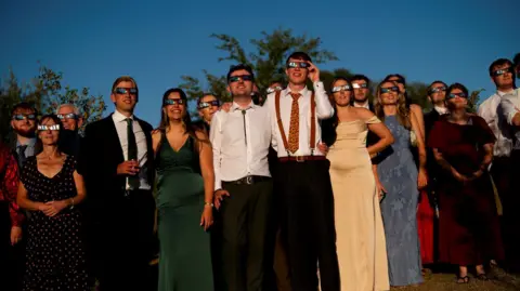 PA Media Jamie and Jerry Bone are surrounded on either side by their guests, all wearing glamorous clothing and special glasses to view the eclipse and protect their eyes.