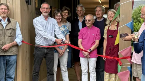 Wiltshire Council A group of about eight older people standing in the entrance to a building with one man holding scissors and about to cut a red ribbon