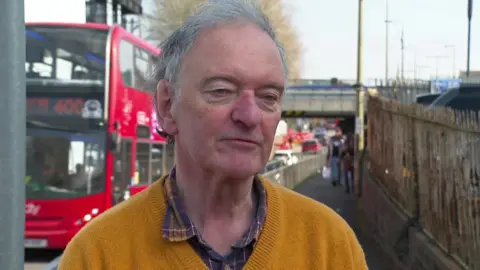 A man wearing a yellow jumper stood in front of a busy main road