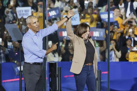 EPA-EFE/REX/Shutterstock Mantan Presiden AS Barack Obama merayakannya dengan mengangkat tangan Kamala Harris di udara dan memberi isyarat ke arahnya di atas panggung pada rapat umum