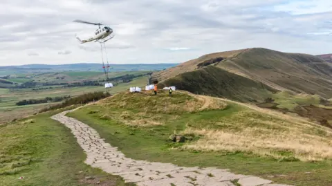 A helicopter airlifting a bag of materials to the top of a hill in the Peak District in Derbyshire 