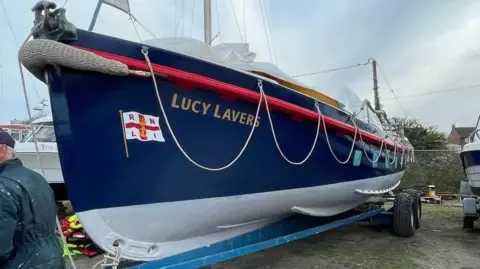 RNLI Lucy Lavers lifeboat on the shore. The boat is white and blue with the RNLI flag on the side.