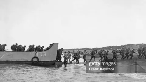Getty Images Black and white photo showing soldiers disembarking a boat and running onto a beach in North Africa.