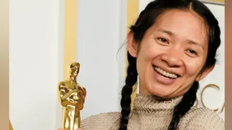 A woman with black hair holding an award.