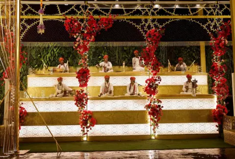 路透社 2024 年 7 月 10 日，在印度孟买商人穆克什·安巴尼 (Mukesh Ambani) 的儿子阿南特·安巴尼 (Anant Ambani) 与拉迪卡·麦钱特 (Radhika Merchant) 的婚礼前，民间音乐家在商人穆克什·安巴尼 (Mukesh Ambani) 的家外表演