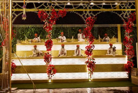 Reuters Folk musicians perform outside the home of businessman Mukesh Ambani ahead of his son Anant Ambani's wedding to Radhika Merchant in Mumbai, India, July 10, 2024