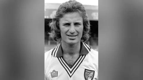 Getty Images A man is wearing a Norwich City jersey and has a mullet. He is looking at the camera.