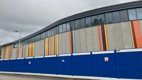 An exterior wall with bands of different colours, including yellow, orange, and burgundy.
