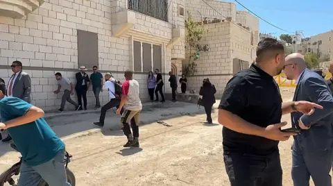 Members of a diplomatic delegation reacting after shots were fired as they gathered at an entrance Jenin camp, some apopear to be running away and others looking behind them 