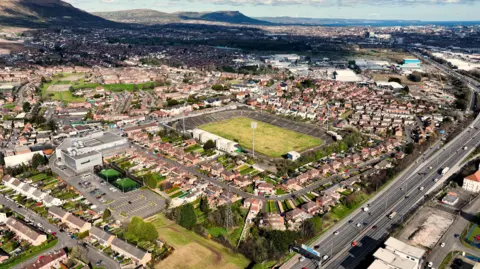 Getty Images An aerial view of a stadium. Houses are surrounding the stadium. Cars are driving on roads. Some are parked. Hills and mountains are in the background.