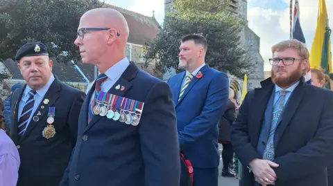 BBC/Stuart Maisner A group of people gather wearing military uniforms. 