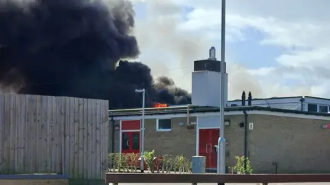 Kev Glen A school building on fire. Thick black smoke billows out of the roof of the building.