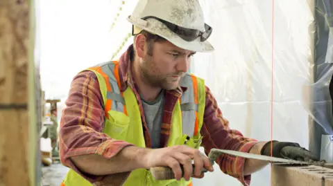 Brick layer on a construction site in a high visibility vest and a hard hat. 
