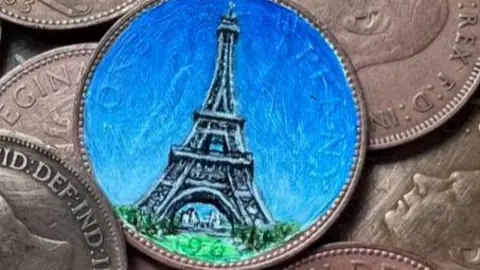 PA Media The Eiffel tower painted on a coin. A blue sky has been painted behind the tower