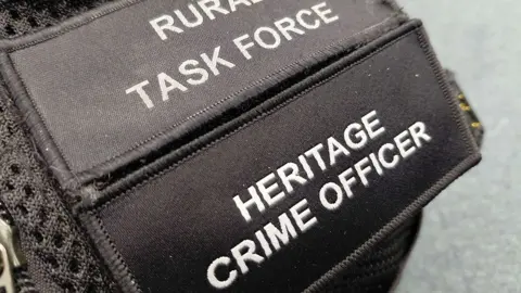 A black shoulder patch on a police officer's uniform which reads "Rural task force" and "Heritage crime officer".