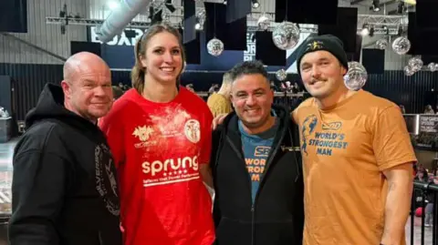 Jade Skill Jade Skill stands in a group with three men and they smile at the camera. The man on the far left is bald and wears a black hoodie. Jade stands next to him wearing a red T-shirt. The man on her right has short dark hair and wears a black zip up hoodie with a blue T-shirt underneath. The man on the far right wears a black beanie hat and yellow T-shirt. 