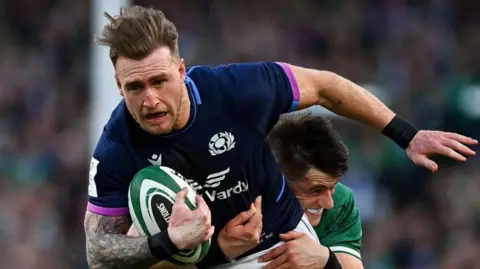 Getty Images Stuart Hogg - who is wearing a Scotland strip and running with a rugby ball - being tackled by an opponent