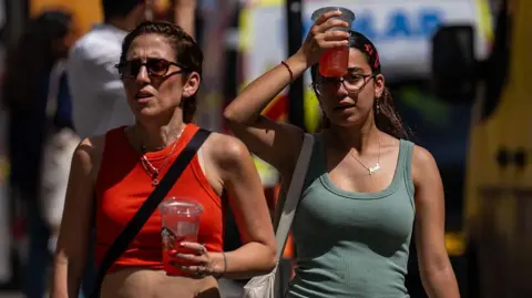 Getty Images A woman cools her head with an iced drink as she walks through central London on a sunny day.