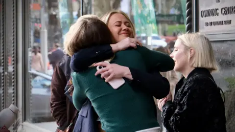 Ethan Rix/ABC News Two women are hugging. They are stood outside a building