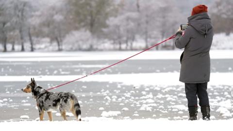 A person photographing a dog by a frozen lake