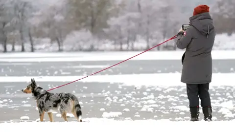 PA Media A person photographing a dog by a frozen lake