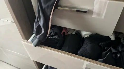 Handout Some messy partially opened drawers in a gloss-effect cream coloured cabinet showing clothing including bras and pyjamas.
