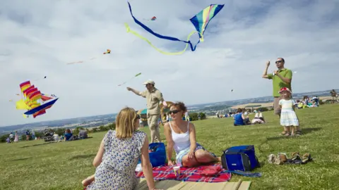 National Trust/Arnhel de Serra Two women sitting on a rug, watching a kite festival with two men holding kites and a child watching too