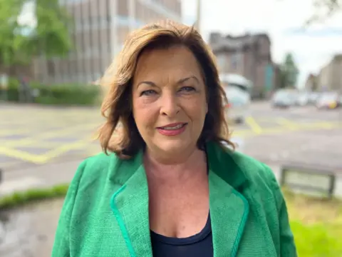 Fiona Hyslop, in a bright green jacket on a busy Edinburgh street