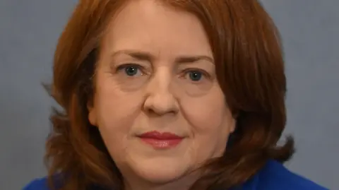 Equality Commission for Northern Ireland A close up of Mary Kitson. She has red hair and red lipstick on. She is wearing a blue jacket. 