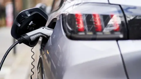 PA Rear view of a grey electric car plugged into a Source London EV charging point