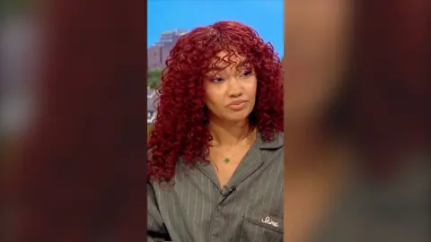 Leigh-Anne Pinnock has curly red hair and wears a grey pinstriped shirt 