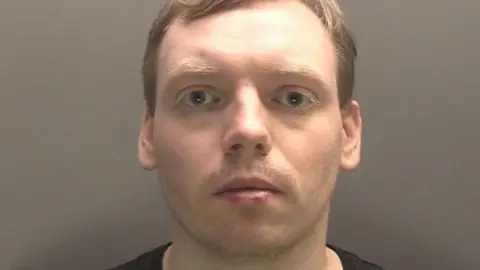 A mugshot of Jonathan Edge, staring straight at the camera wearing a black t-shirt.