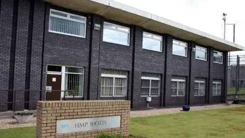 A large prison building. HMP Shotts is written on a sign outside the building.