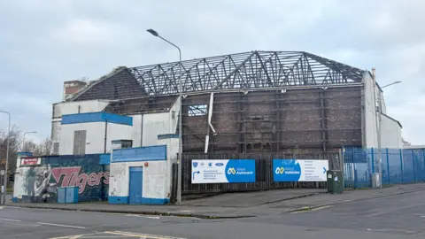 A side angle of the art deco style building, showing the metal frame work of where the roof and back wall used to be.